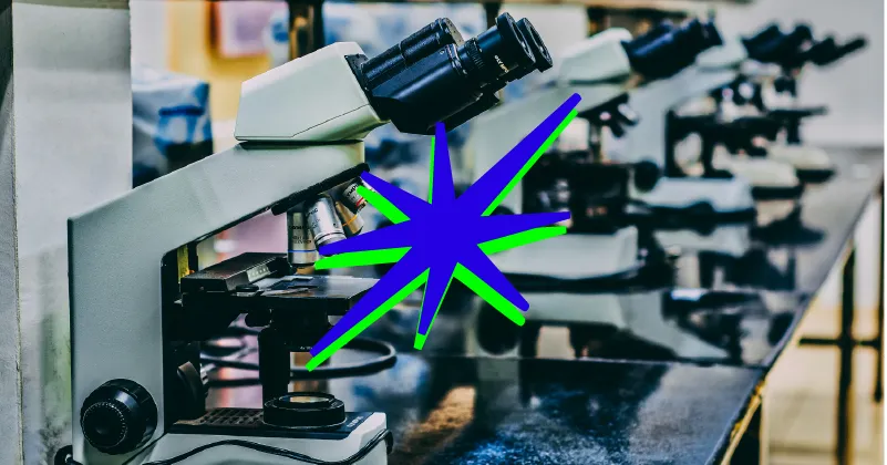 Useita mikroskooppeja valkoisella laboratoriopöydällä. Yhdessä mikroskoopissa on sinivihreä tähti, taustalla sumennus.